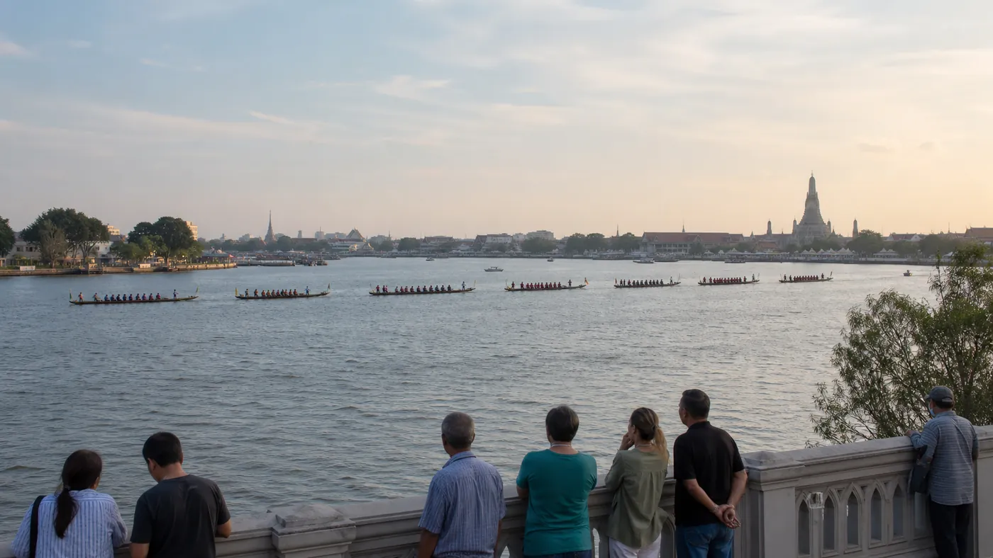 Wide view of coordinated ceremonial rowing boats on the Chao Phraya with Wat Arun in the distance and spectators at the riverbank